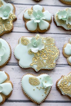 many decorated cookies are arranged on a white wooden table with gold trimmings and flowers