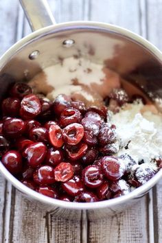 cherries are mixed together in a saucepan on a wooden table with spoons