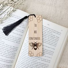 an open book with a wooden bookmark that says 10 bee confined and a black tassel hanging from it