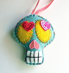 a blue and yellow sugar skull ornament hanging from a pink ribbon on a white surface