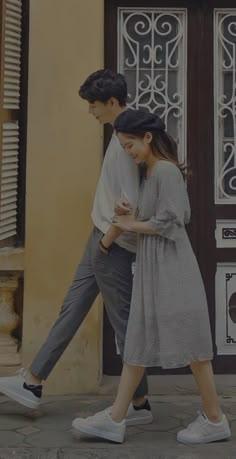 a man and woman are walking down the street with their cell phones in hand as they look at each other