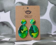 a pair of green and yellow earrings sitting on top of a cardboard card board next to a wall