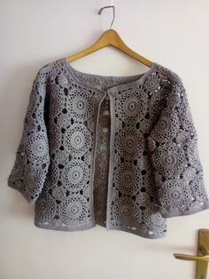 a gray crocheted sweater hanging on a wall next to a coat hanger