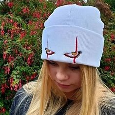 a woman with long blonde hair wearing a white knitted hat with evil eyes on it