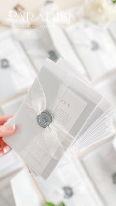 a person holding several envelopes in front of a bunch of white flowers on a table