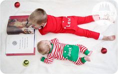 a baby laying on the floor next to a book and christmas ornaments, with a little boy in red pajamas