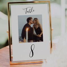 a table number frame with a couple kissing in front of a candle on top of a wooden table