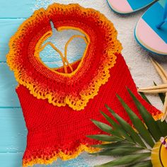 a red and yellow crocheted sweater next to flip flops