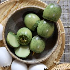 a bowl filled with green apples next to an egg on top of a bamboo mat