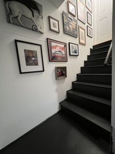 there are many pictures on the wall next to the stairs in this house with black carpet