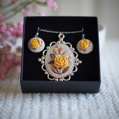 a necklace and earring set in a box on a table with flowers behind it