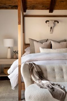 a bed with white sheets and pillows in a bedroom next to a cow skull on the wall