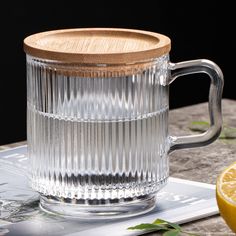 a glass mug with a wooden lid sitting on top of a table next to a lemon