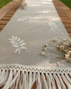 a table runner with white flowers and tassels on top of it, sitting on a picnic table