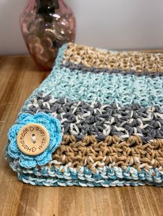 a crocheted blanket with a wooden button on the end and a vase in the background