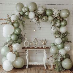 an arch made out of balloons and greenery on a table in front of a white wall