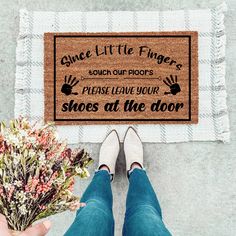 someone holding flowers in front of a door mat that says, once little fingers touch our doors please leave your shoes at the door