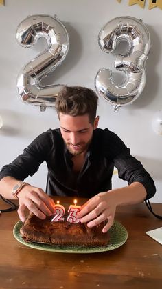 a man lighting candles on a cake with the number twenty three in front of him