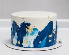 a white and blue cake with gold leaf decorations on it's side, sitting on a table