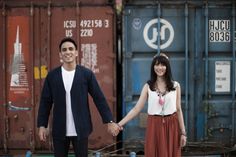 a man and woman holding hands in front of shipping containers