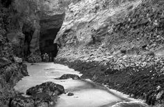 black and white photograph of people standing at the entrance to a cave