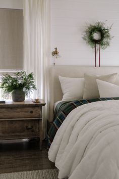 a bed with white comforter and pillows in a bedroom next to a dresser, potted plant and window