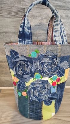 a handbag made out of old jeans with flowers on the front and sides, sitting on a wooden surface