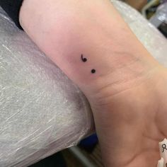 a small black dot tattoo on the wrist