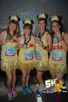 four women in yellow dresses holding medals and posing for the camera with mickey mouse ears on their heads