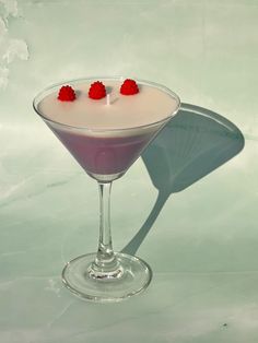 a martini with raspberries in it on a white tablecloth and a shadow