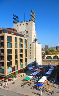 people are walking around in front of a building with tents on the roof and tables set up outside