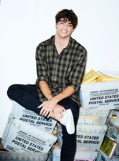 a young man sitting on top of stacks of mail and boxes smiling at the camera