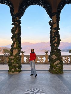 a woman is standing in front of an ornate structure with arches and pillars, looking at the camera