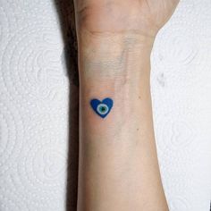 a small blue heart with an evil eye tattoo on the left wrist and right arm