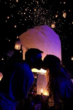 two people are kissing in front of some paper lanterns at night with the sky lit up