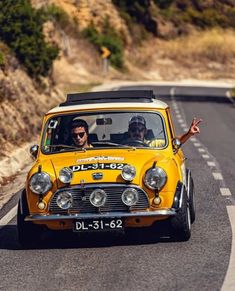 an old yellow car driving down the road with two men in it's cab