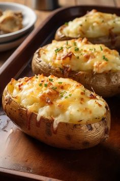 baked potatoes with cheese and parmesan on a wooden serving tray next to a bowl