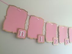 pink and gold paper tags hanging from a line on a wall with numbers in the middle