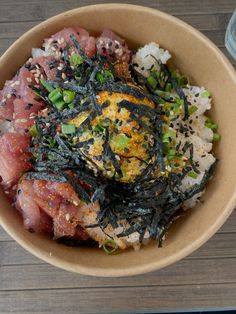 a bowl filled with rice, meat and vegetables on top of a wooden table next to a drink