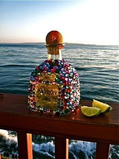 a bottle of liquor sitting on top of a wooden table next to the ocean with a slice of lime