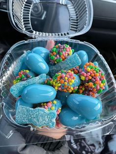 a plastic container filled with lots of blue and yellow candy covered rocks next to a car steering wheel