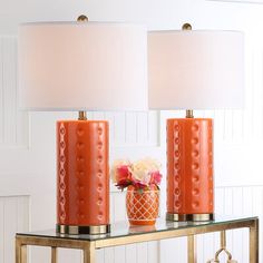 two orange lamps sitting on top of a glass table next to a vase with flowers