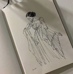 a drawing of a woman's dress on top of a white book with black ribbon