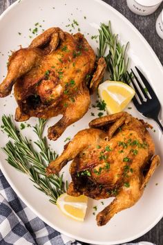 two chicken legs on a plate with lemon wedges and rosemary garnishes