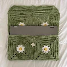 a green crocheted laptop case with flowers on the front and side, sitting on a bed