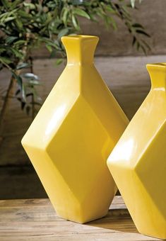 two yellow vases sitting next to each other on top of a wooden table in front of a potted plant