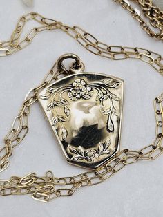 This is a "once in a lifetime" piece of estate jewelry.  This would make a lovely, thoughtful gift for your sweetheart. This very special antique locket necklace is made of highly polished solid yellow gold.  The locket is 10K and the chain is 14K.  Both are stamped accordingly. The locket has a unique shield shape which has a beautiful floral forget-me-not design on the front and a monogram on the back.  The locket is a little over one inch long.  The inside still holds the original black and white portrait of a handsome gentleman.  The photo is held in place by the original frame and cover.  I imagine there is a wonderful love story attached to this piece.  The necklace is a mini paperclip style chain with a spring ring clasp.  The clasp is stamped 585 (14K).  The chain is 18 inches long Gold Custom Necklace For Anniversary, Formal Jewelry With Polished Flower Pendant, Formal Flower Pendant Jewelry With Polished Finish, Formal Polished Flower Pendant Jewelry, Heirloom Oval Jewelry For Valentine's Day, Heirloom Heart-shaped Yellow Gold Jewelry, Formal Necklace With Polished Flower Pendant, Heirloom Jewelry For Valentine's Day, Anniversary Brass Jewelry With Polished Finish