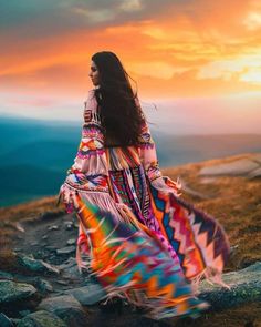 a woman in a colorful dress standing on top of a hill