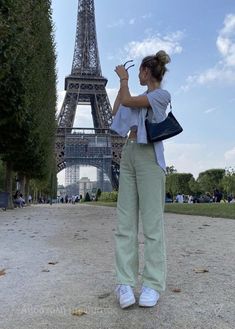 a woman standing in front of the eiffel tower taking a photo with her cell phone