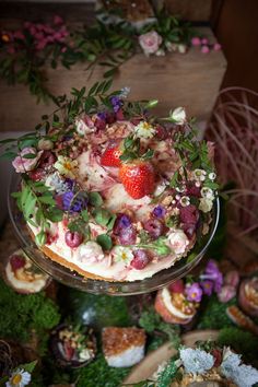 a cake with strawberries and flowers is on a glass platter next to other desserts